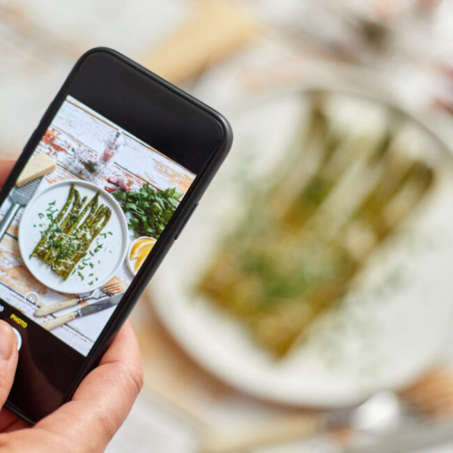 Woman taking picture of fresh prepared food with smartphone for social media. Roasted aparagus. Woman taking picture of fresh prepared food with smartphone for social media. Roasted aparagus with herbs and parmesan.